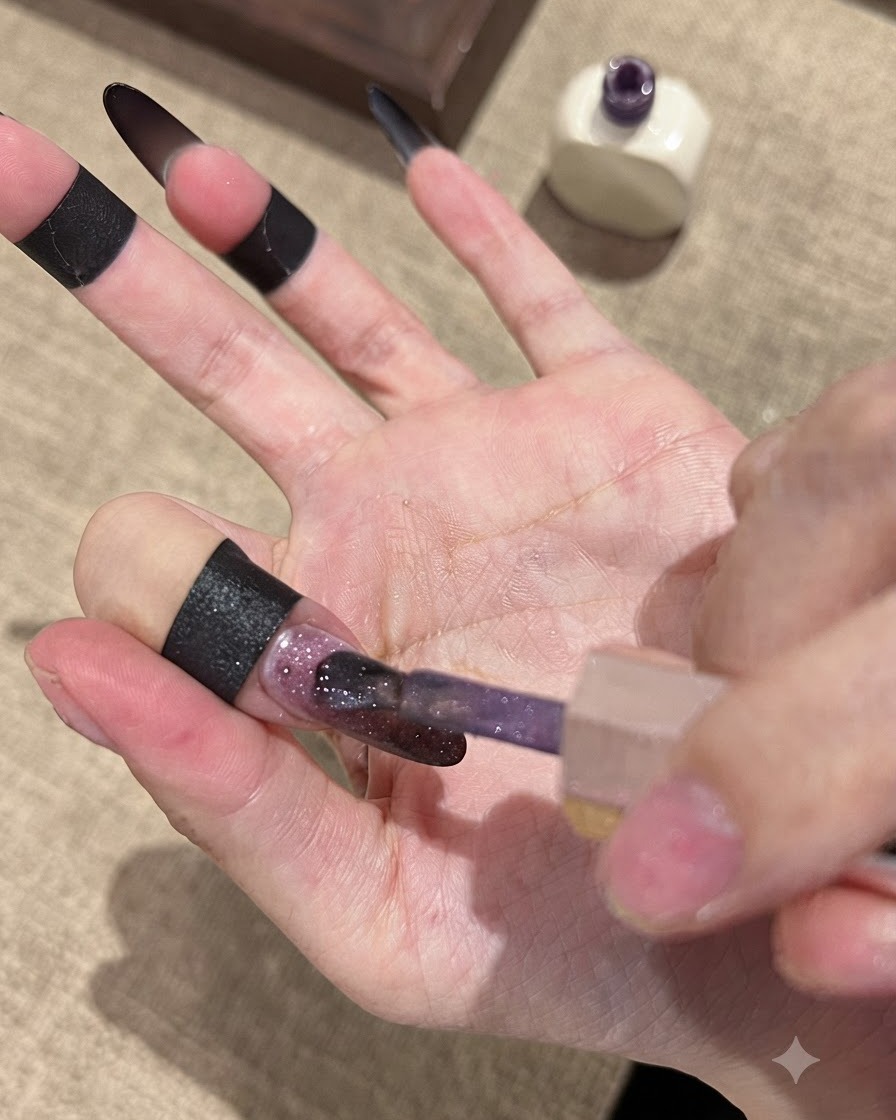 Un pinceau appliquant le vernis en gel Fallen Gold Cat Eye sur une base dongle dégradée sombre.