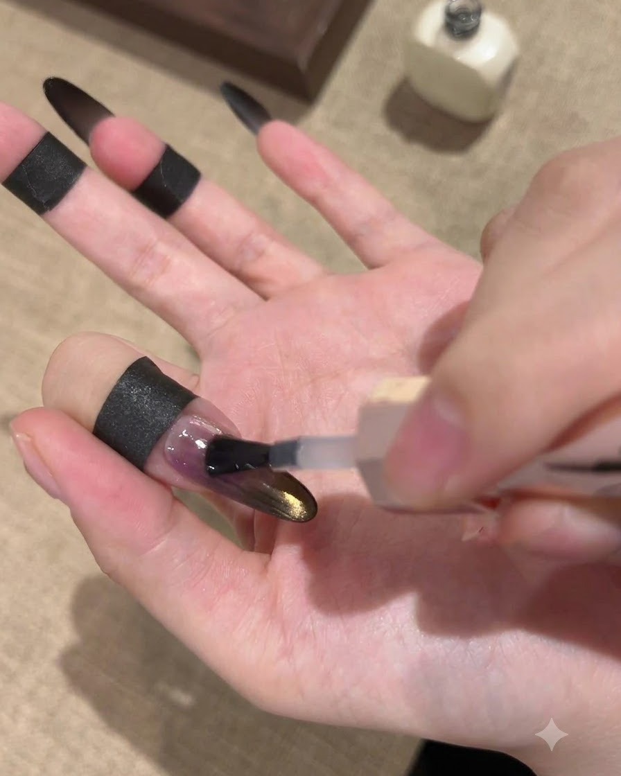 Un pinceau appliquant un top coat scellant brillant sur un ongle dégradé noir et or avec effet œil de chat.