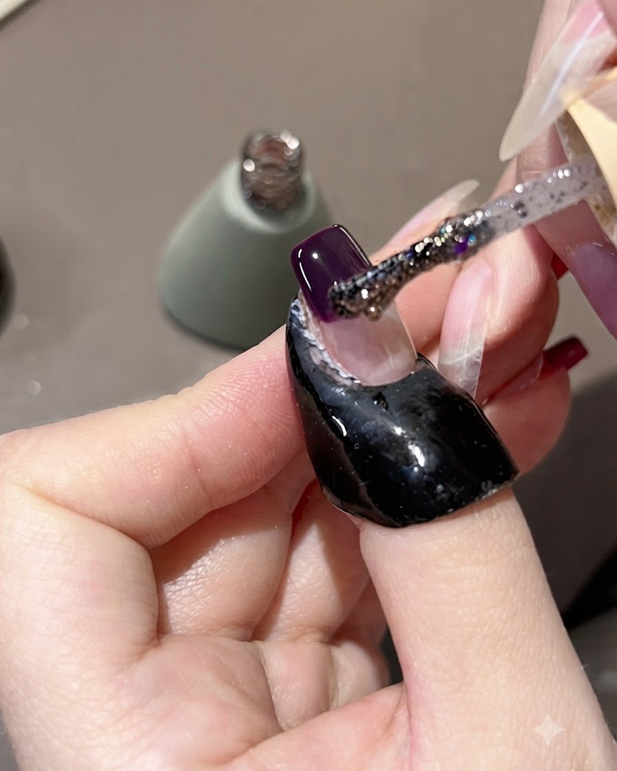 Un pinceau appliquant du gel à paillettes violettes sur une pointe dongle violette foncée, en létirant légèrement vers le haut.