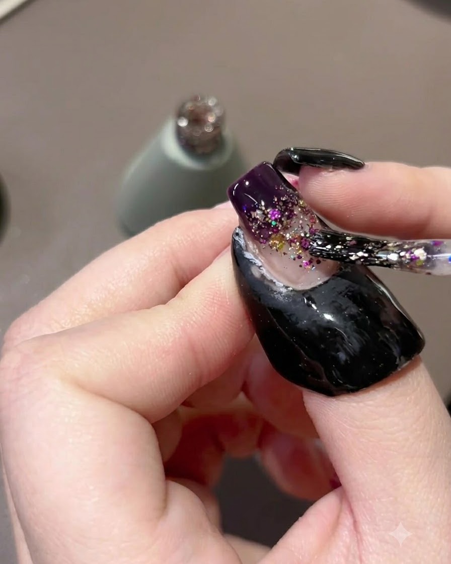 Un pinceau à ongles tapotant et étirant les particules de paillettes violettes le long de longle pour former un dégradé.