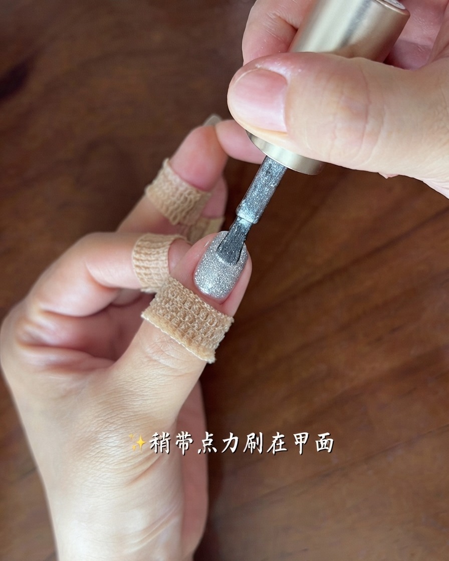 Un pinceau appliquant une fine couche scintillante de gel œil de chat gris argenté sur un ongle.