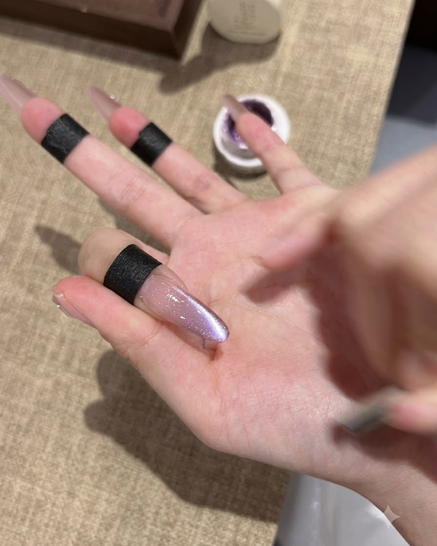 Gros plan dun ongle en amande allongé montrant un vernis gel œil-de-chat violet fraîchement fixé avec un centre réfléchissant scintillant.