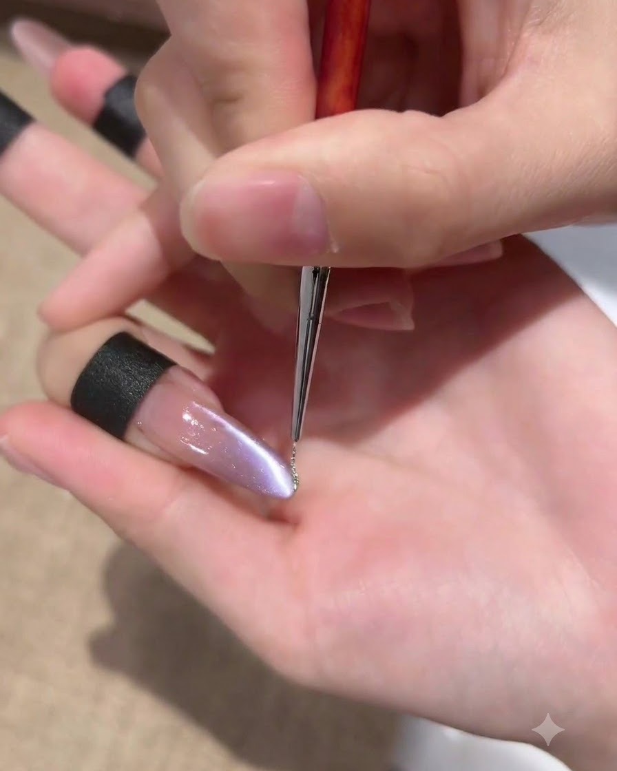 Un pinceau liner fin appliquant une ligne très fine de gel pailleté argenté le long du flanc dun ongle œil-de-chat violet.