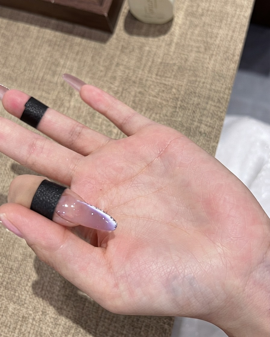 Un pinceau appliquant un top coat ultra-brillant final sur un ongle ombré œil-de-chat violet bordé de fines paillettes argentées.