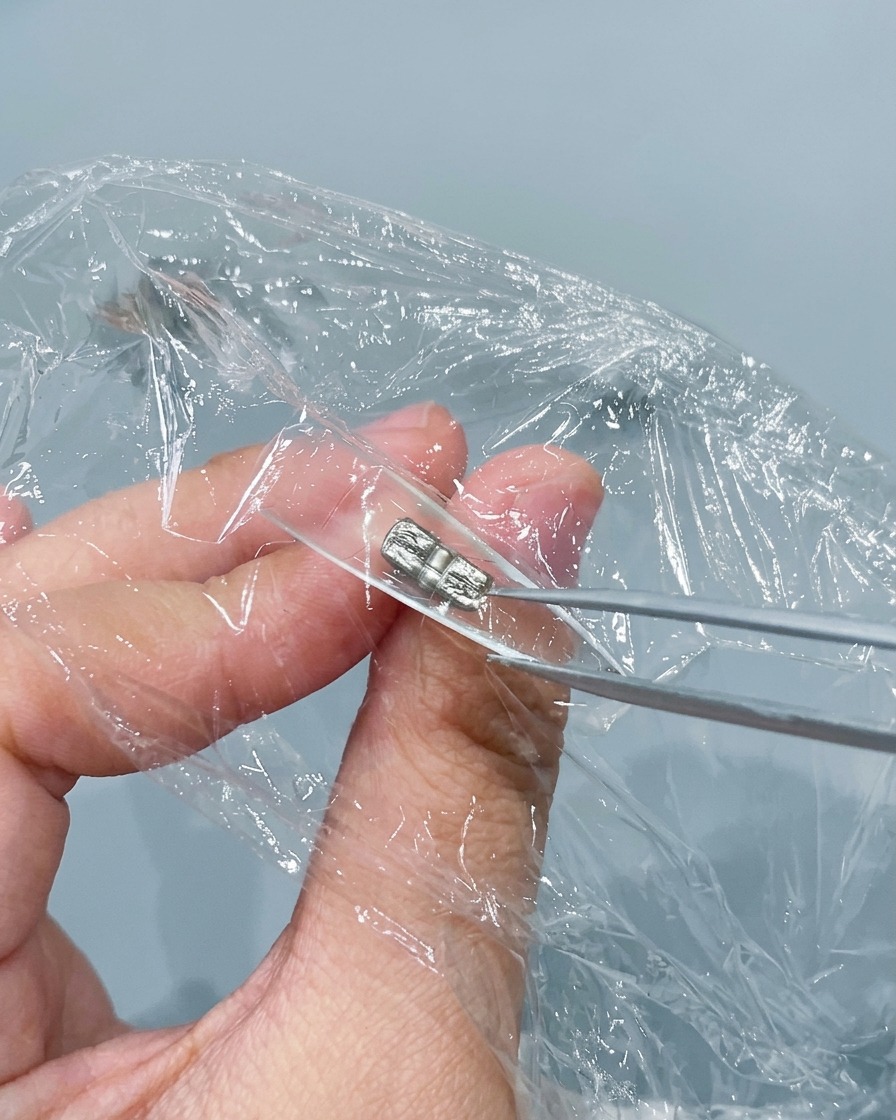 Une paire de pinces métalliques pinçant et froissant du film plastique pressé à lintérieur dune capsule dongle transparente.