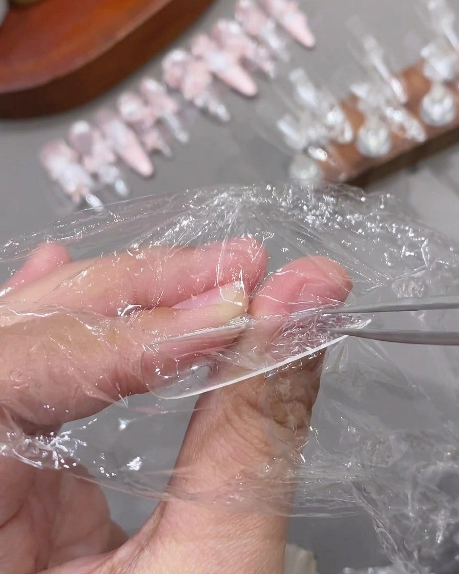 Une paire de pinces retirant un film plastique dune capsule dongle transparente texturée et catalysée.