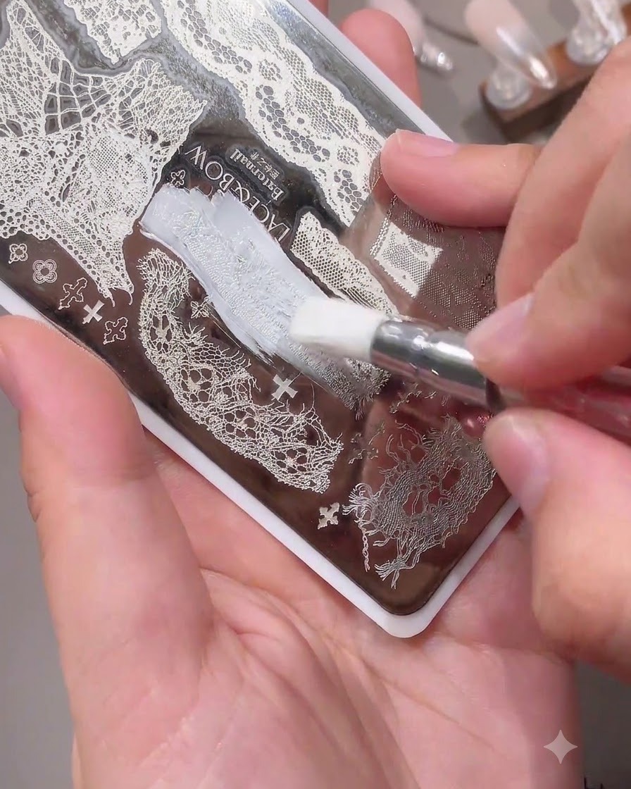 Un pinceau appliquant du vernis blanc sur un motif de dentelle délicat sur une plaque de stamping pour ongles en métal.