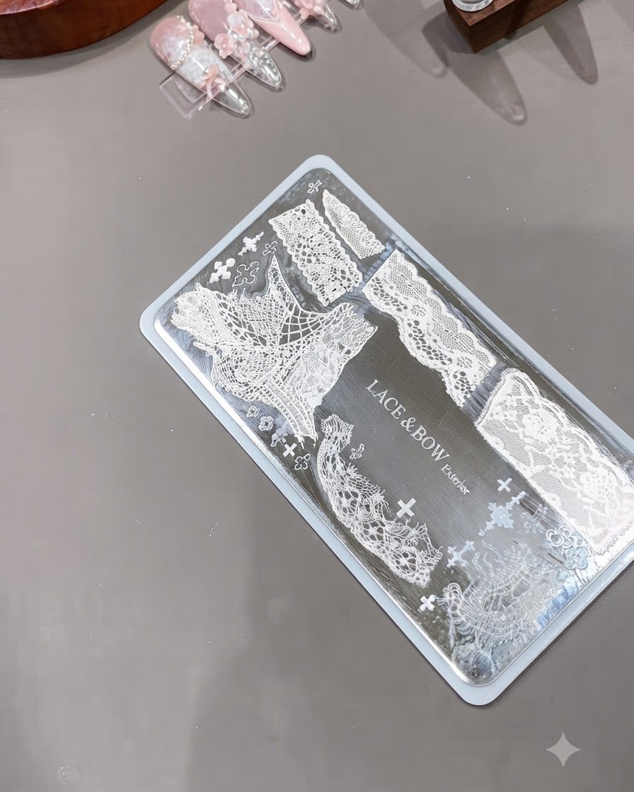 Un tampon dongle en silicone transparent positionné à côté dune plaque métallique gravée affichant des motifs de dentelle blanche complexes.