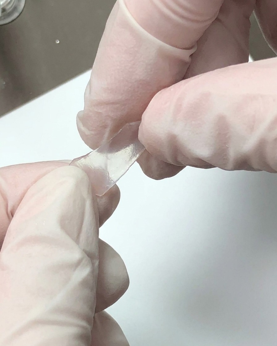 Des mains gantées brisant une feuille décorative translucide en petits fragments.