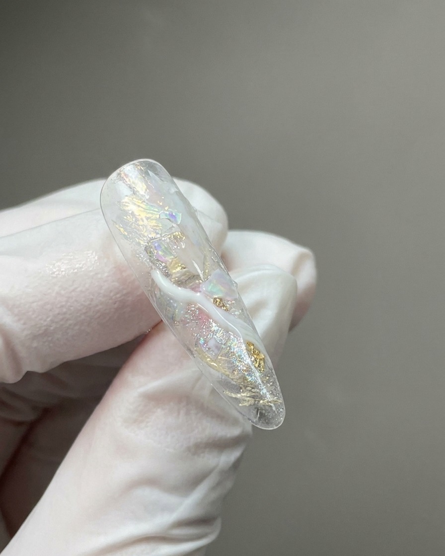 Gros plan sur une capsule dongle transparente présentant des flocons scintillants incrustés et des volutes de détails marbrés blanc laiteux.