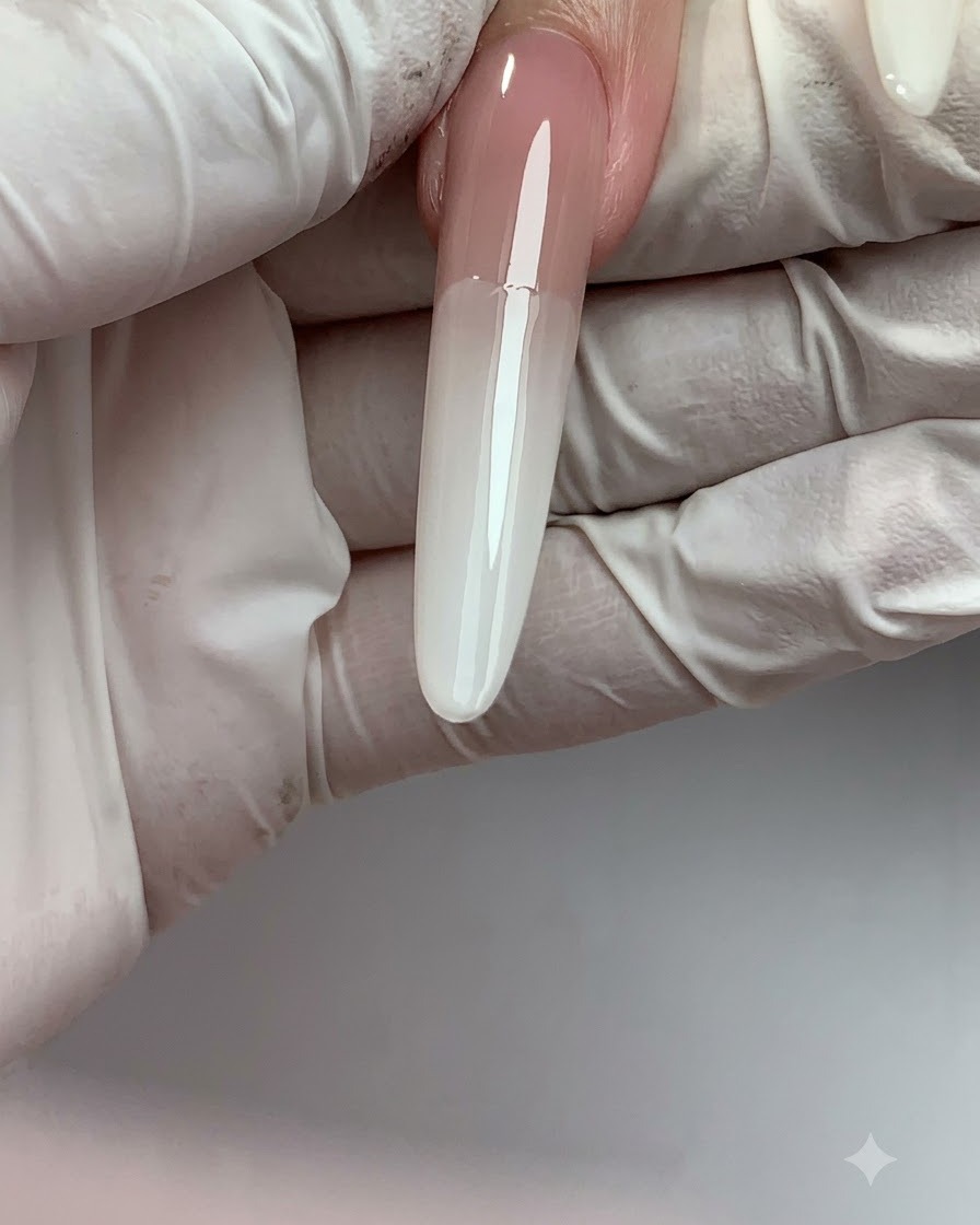 Un ongle long en extension présentant une transition ombré fluide entre le nude en haut et le blanc lait à la pointe.