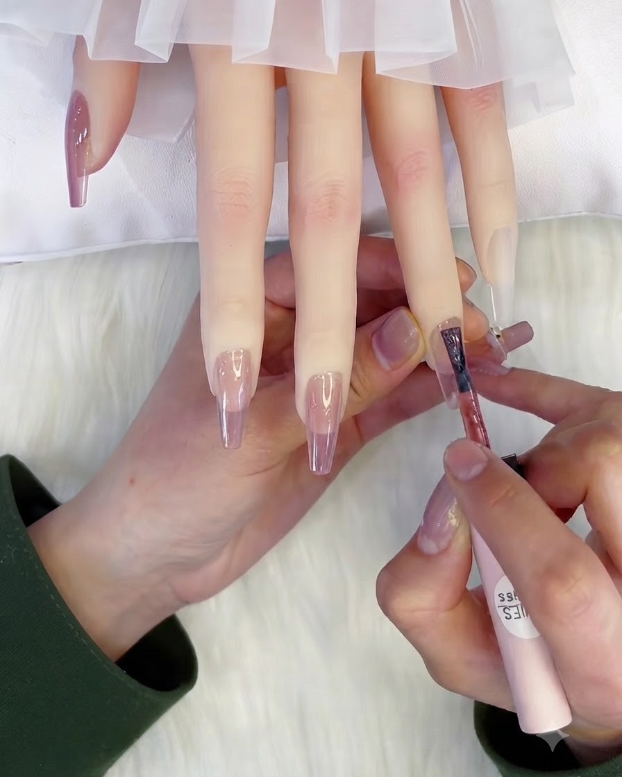 Un pinceau appliquant une seconde couche de vernis gel rose translucide sur un ongle.