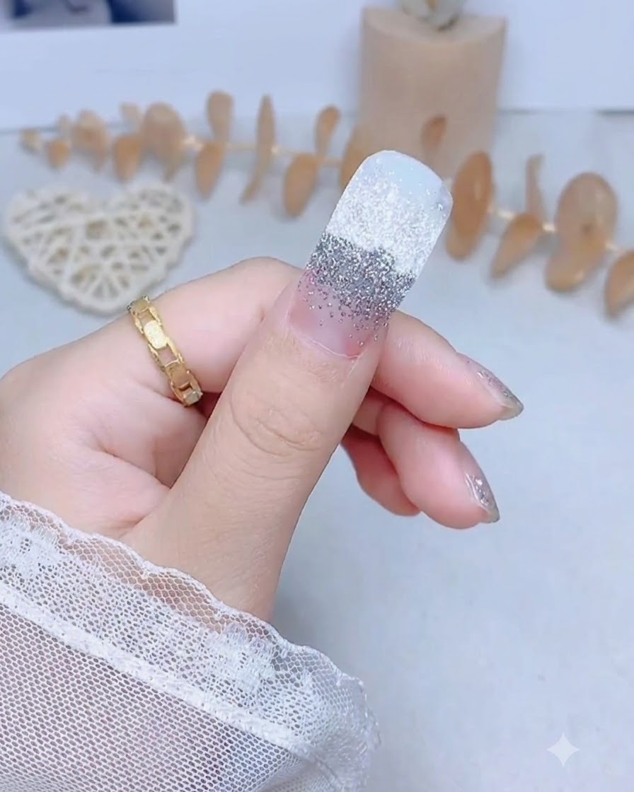 Un ongle de pouce avec un autocollant pailleté argenté fermement pressé au centre.
