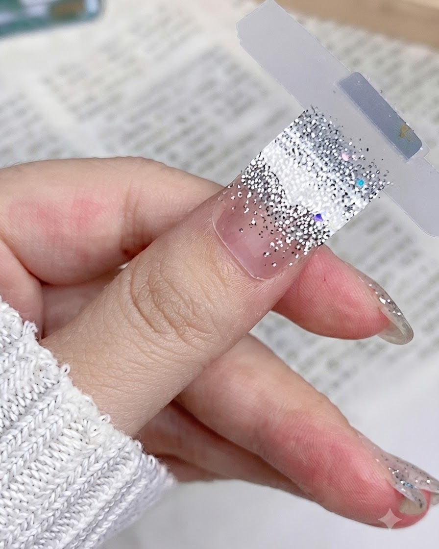 Gros plan dun sticker dongle pailleté argenté placé à plat et de manière lisse sur un ongle de pouce naturel.