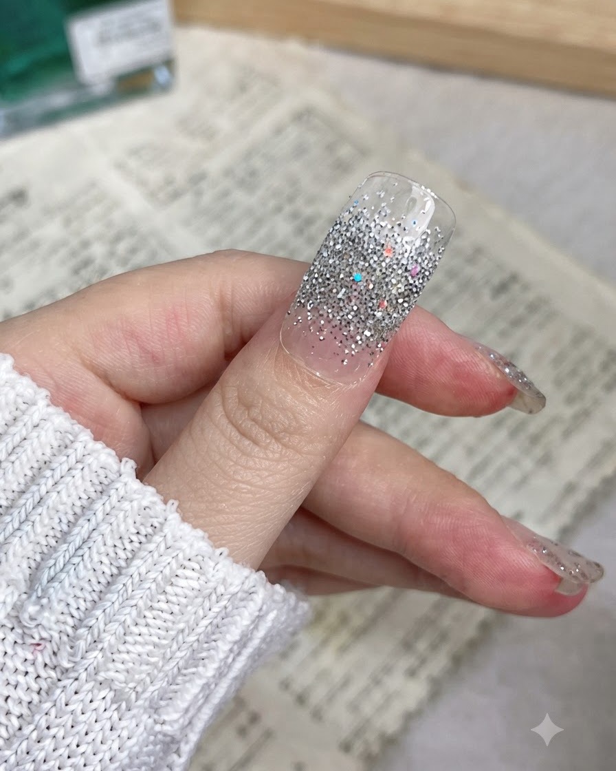 Gros plan dun pouce avec un wrap dongle pailleté argenté appliqué en douceur de la cuticule jusquau bord.