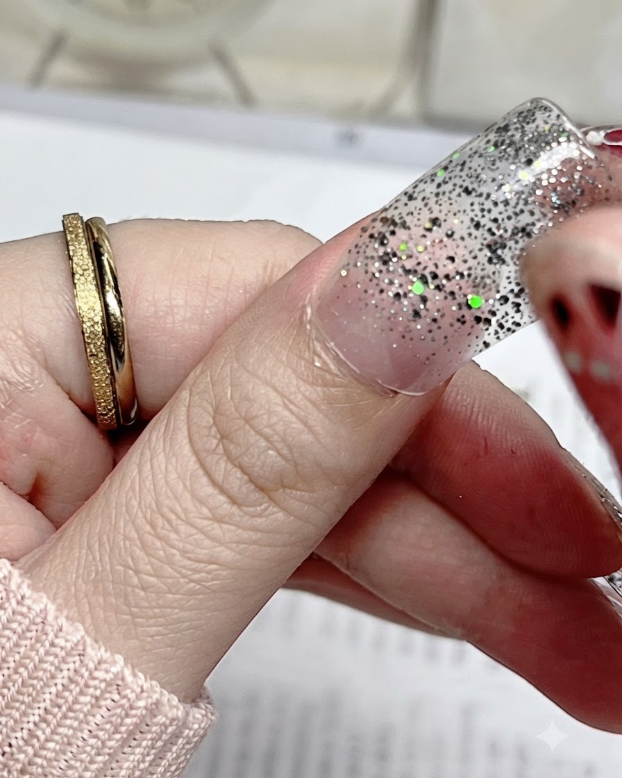 Un gros plan dun sticker dongle à paillettes argentées aligné précisément avec la cuticule dun ongle de pouce naturel.