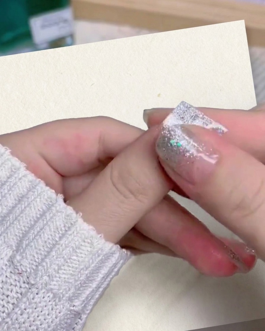 Gros plan du pouce et de lindex dune personne pressant et lissant fermement un faux ongle en dégradé pailleté sur son doigt.