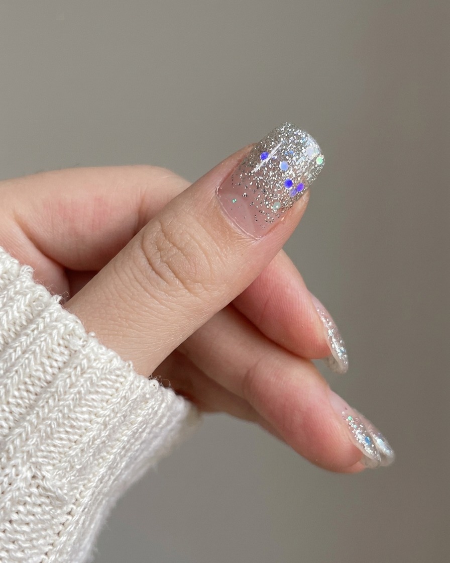 Gros plan montrant le nouvel ongle en dégradé pailleté argenté posé sur lindex à côté dongles non vernis.