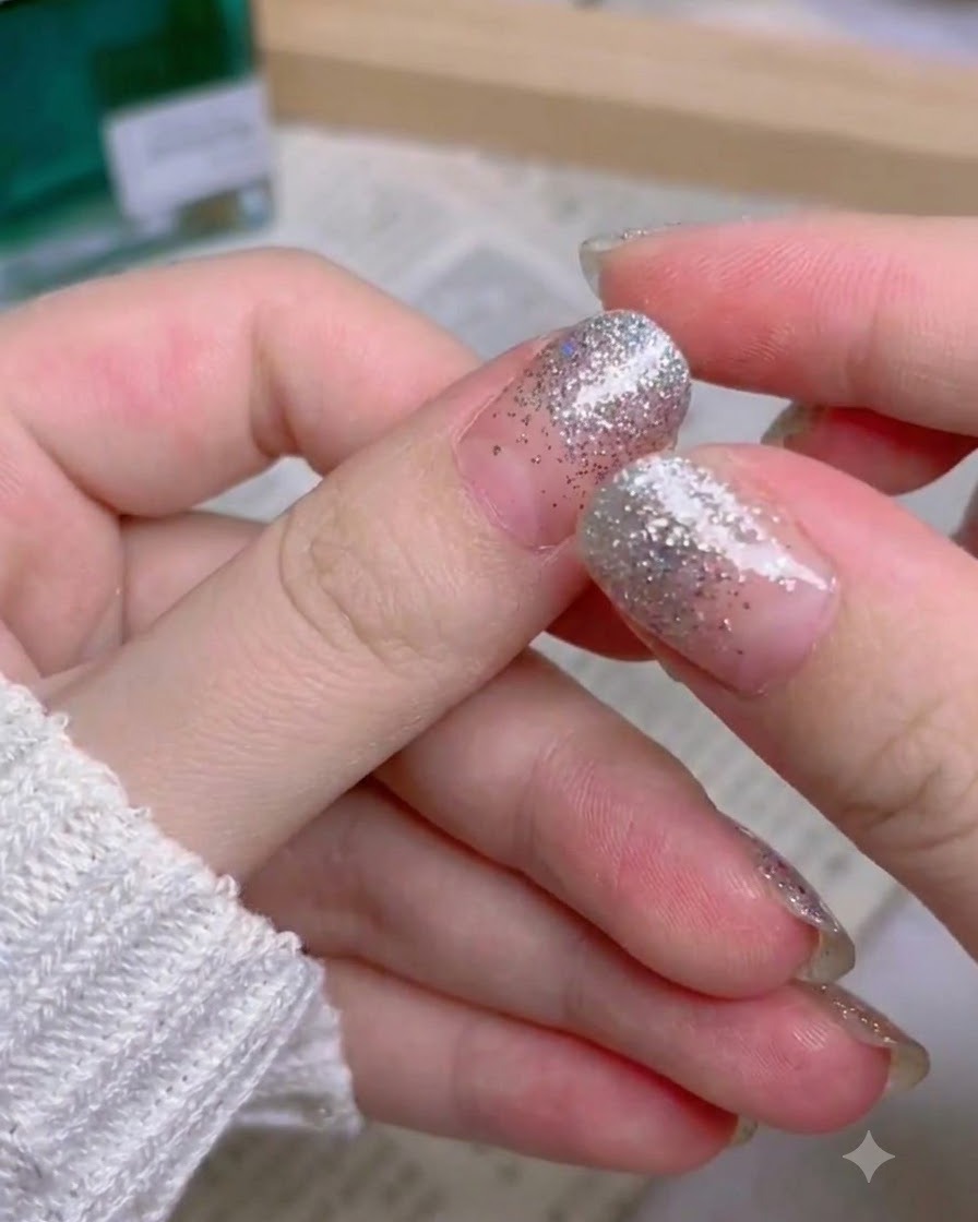 Une main montrant lensemble complet des ongles press-on en dégradé de paillettes argentées.