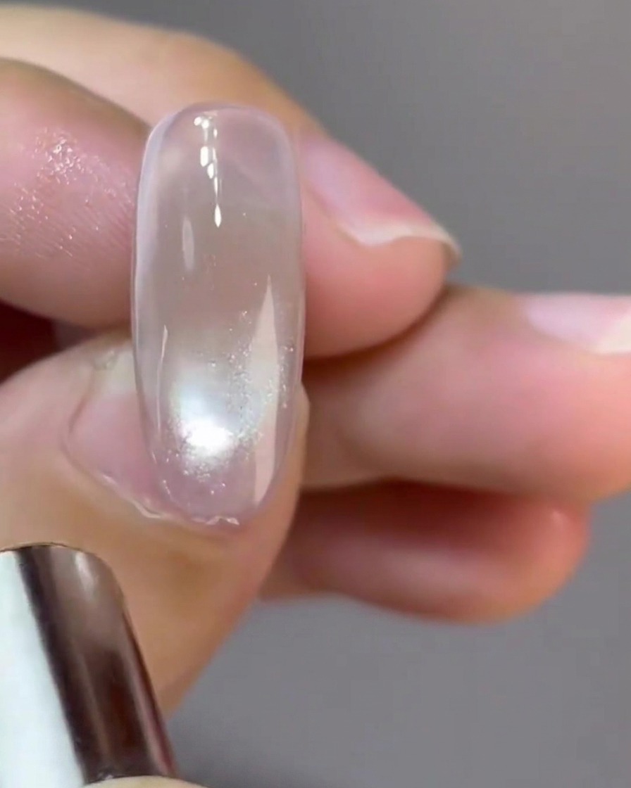 Un petit aimant circulaire façonnant un reflet en forme de boule de verre sur un ongle.