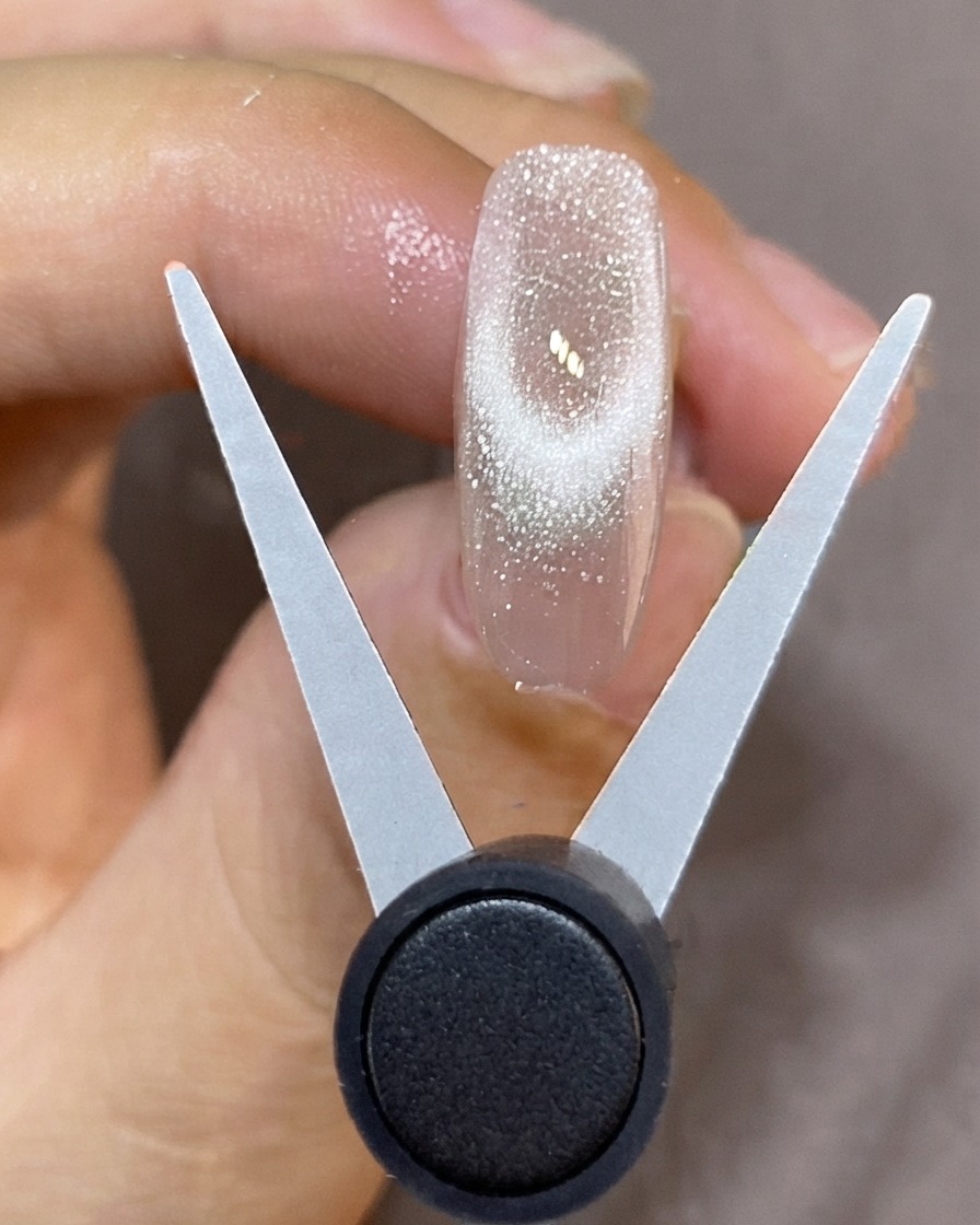 Un outil magnétique en forme de V tenu au-dessus dun ongle translucide pour créer une French scintillante en cat-eye.
