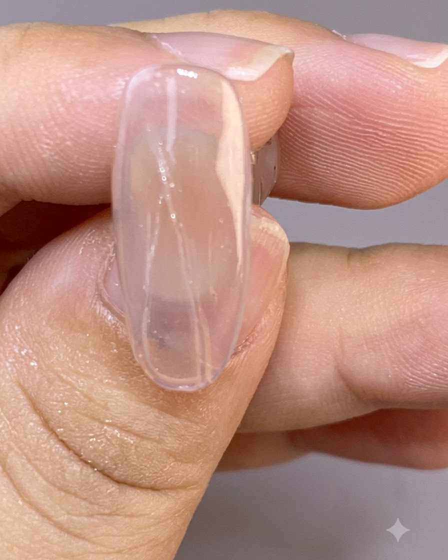 Un gros plan dun ongle transparent montrant de fines lignes délicates peintes en forme de plumes sur la surface humide.