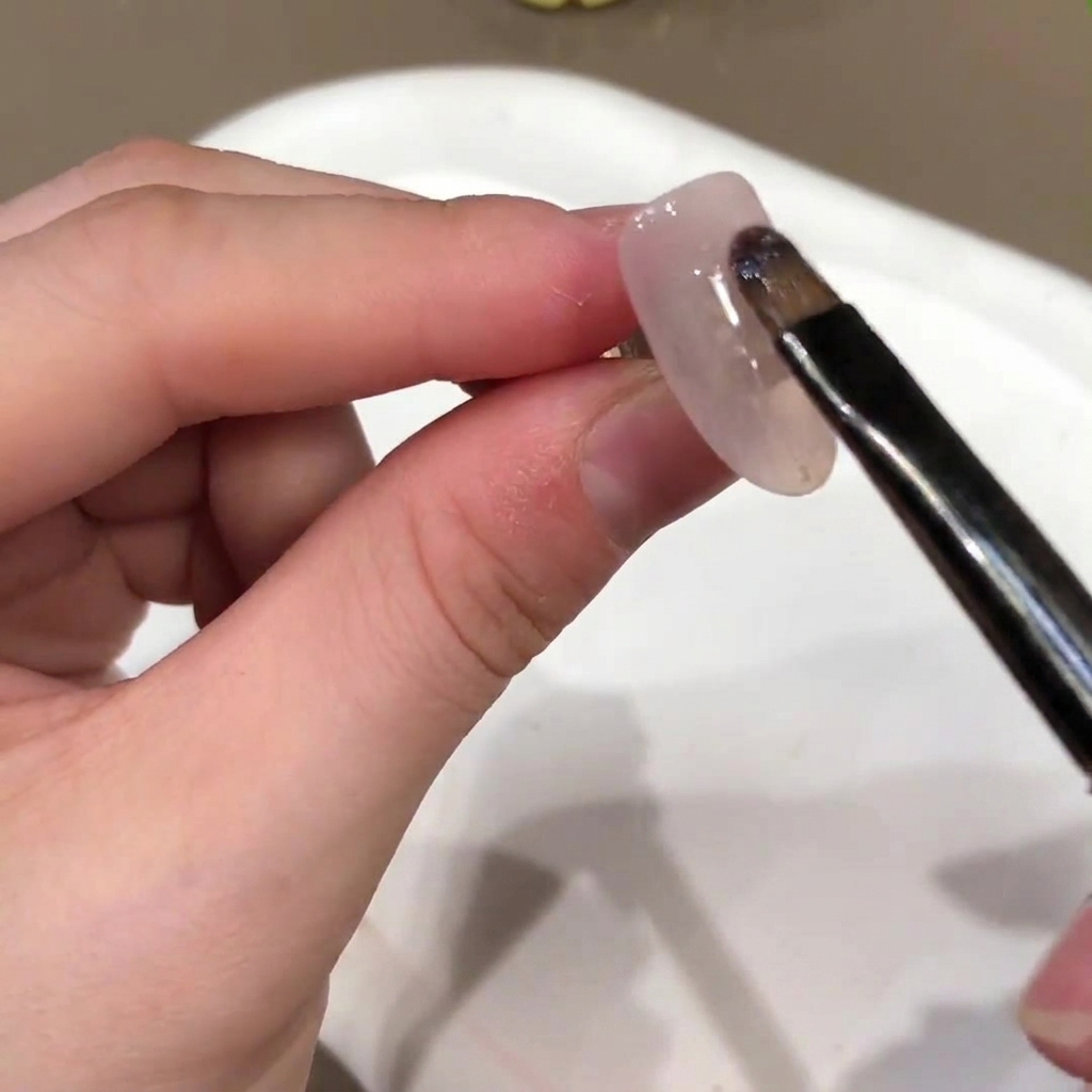 Un pinceau à ongles appliquant une couleur de base en gel rose nude sur la surface dun ongle artificiel.