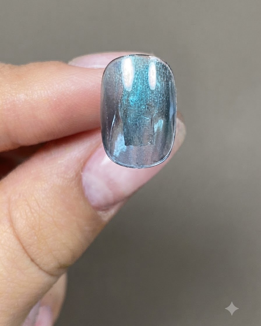 Un pinceau à ongles appliquant une couche épaisse de gel cat eye bleu-vert sur un ongle artificiel.