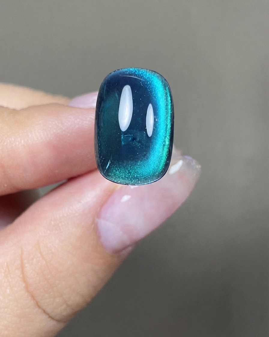 Un ongle cat eye bleu-vert montrant une bande lumineuse verticale large et centrée.