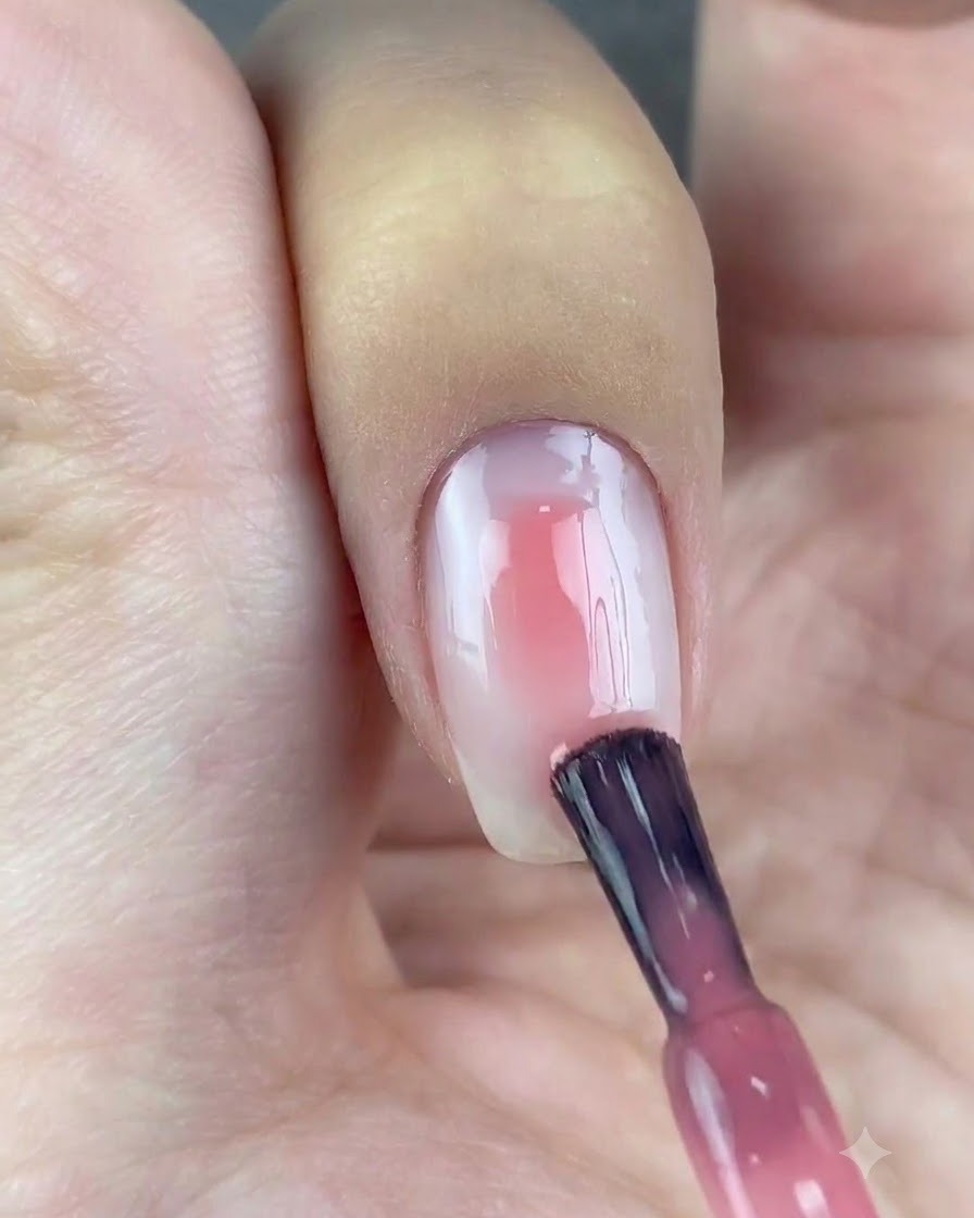 Un pinceau appliquant une touche de gel rose translucide au centre dun ongle à base blanche.