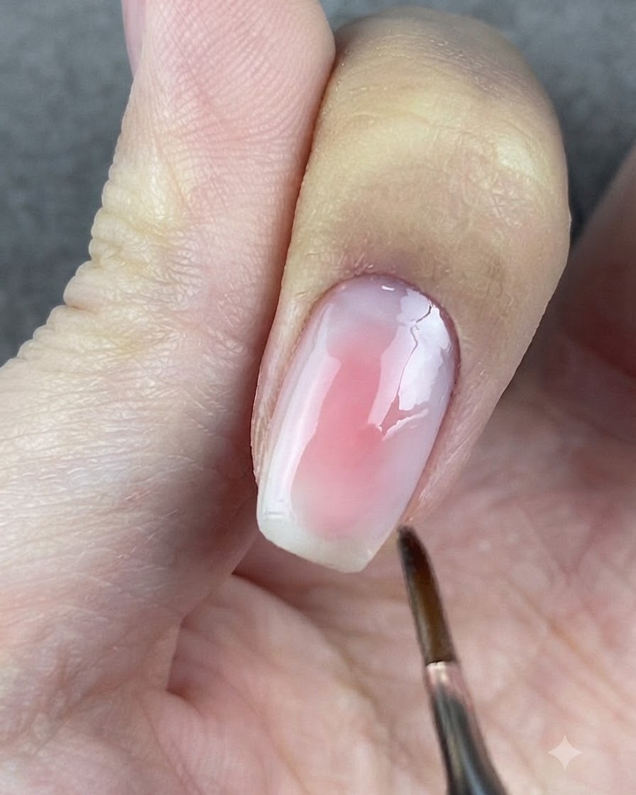 Un pinceau rond tapotant délicatement les bords du gel rose sur un ongle.