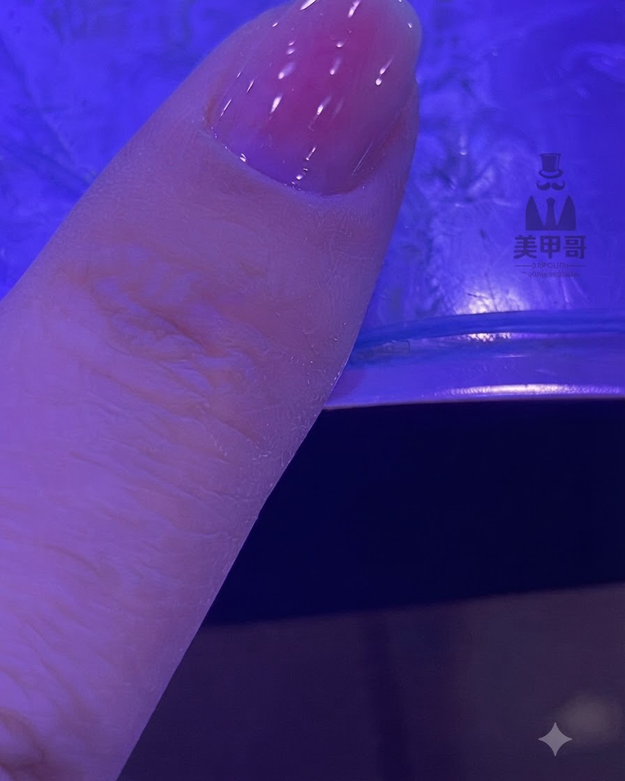 Un ongle avec un dégradé rose estompé en train de catalyser sous une lampe UV ou LED.
