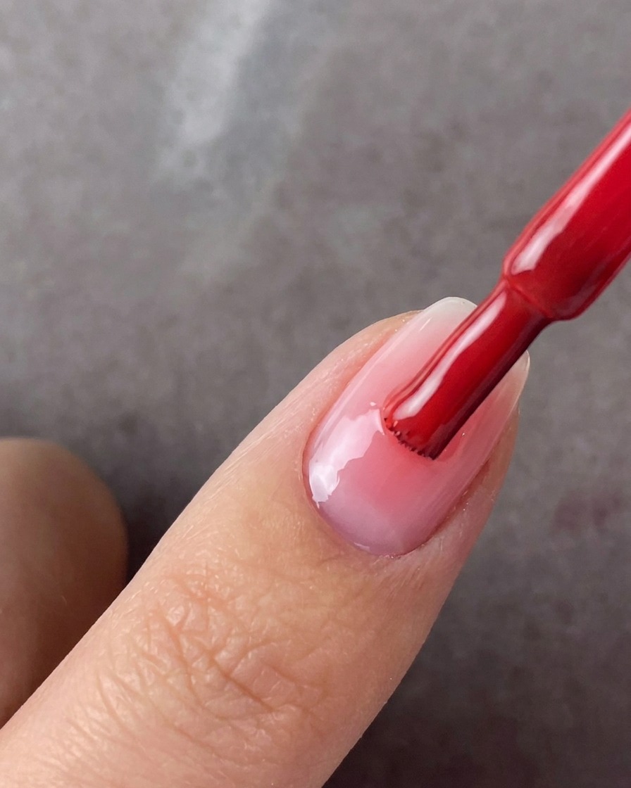 Un pinceau appliquant une deuxième couche de gel rose au centre dun ongle manucuré.
