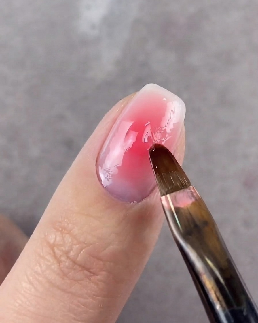 Un pinceau rond floutant les bords du point central sur un ongle.