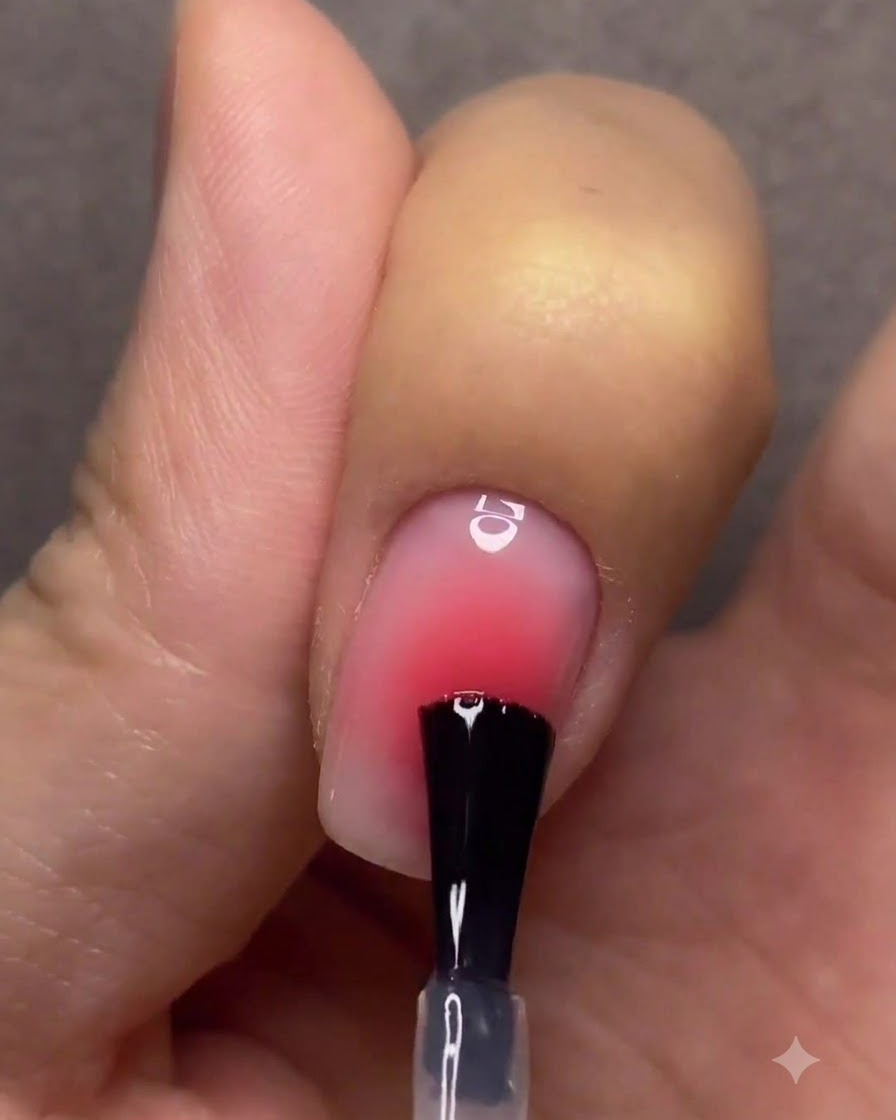 Une main avec des ongles dégradés finis catalysant sous une lampe à ongles rose UV ou LED.