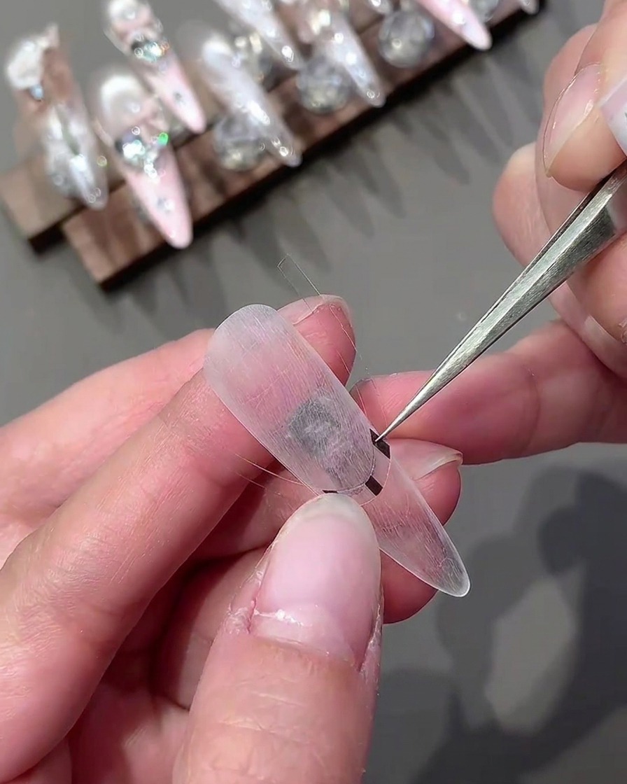 Une pince à épiler plaçant un autocollant incurvé horizontalement sur une capsule transparente.