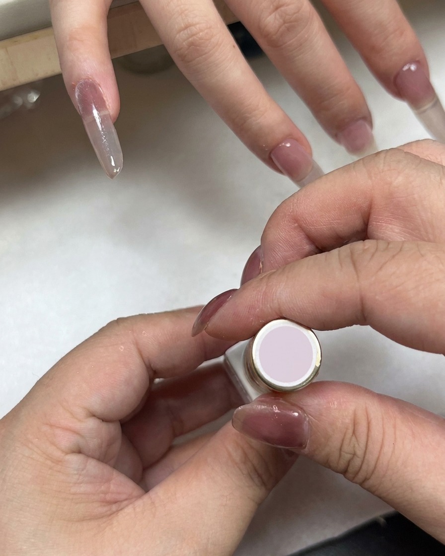Un flacon de vernis à ongles avec un capuchon rose clair tenu près dune main aux ongles dégradés.