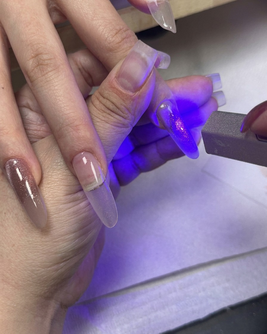Une lumière UV catalysant un ongle peint tandis que dautres doigts avec du gel œil de chat en dégradé reposent à proximité.