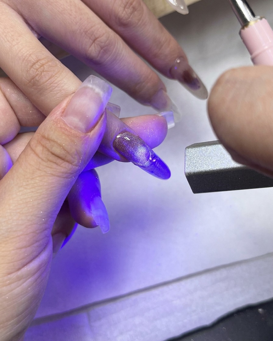 Une lampe de catalysation UV/LED pointée directement sur le majeur mettant en valeur la french manucure texturée.