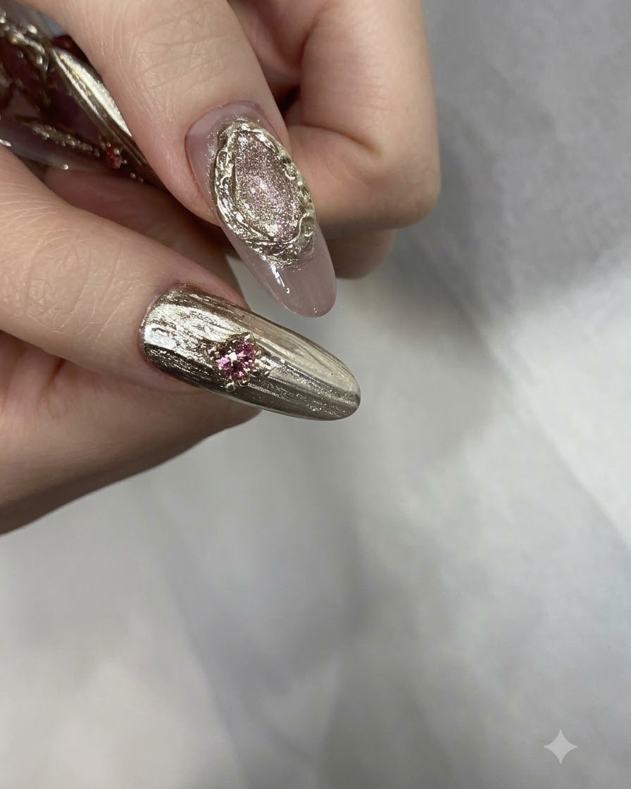 Doigts manucurés terminés ornés de strass roses, de perles dorées et de détails chromés texturés.