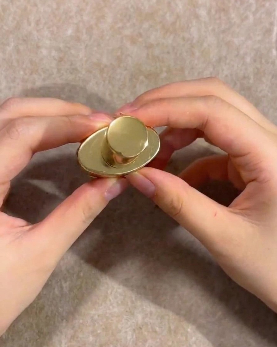 Mains tenant le capuchon doré dun flacon de vernis gel nude.
