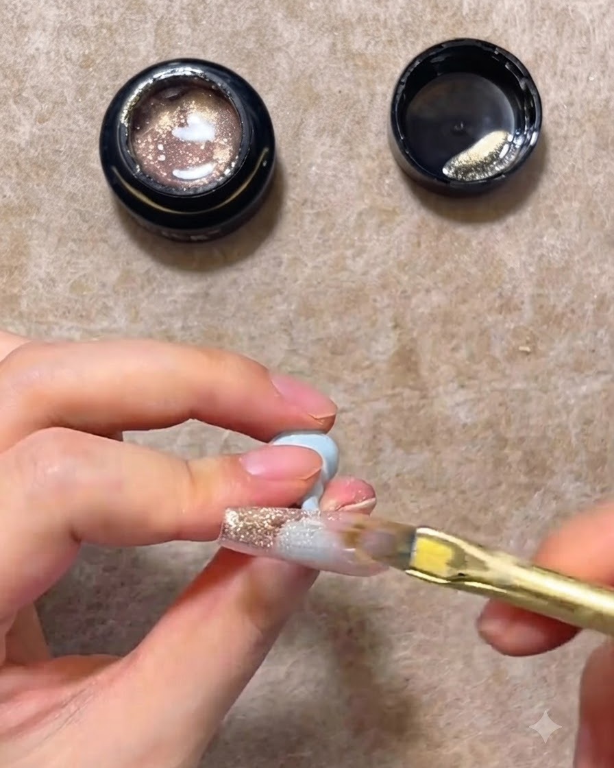 Un pinceau à ongles plat balayant le gel cat eye rose or vers le bas dune capsule dongle transparente pour créer un dégradé.