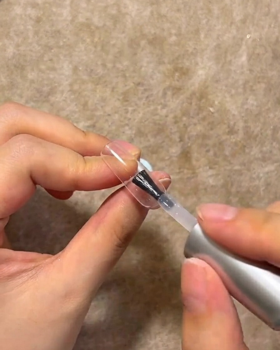 Un pinceau à ongles appliquant une couche de gel de construction transparent sur la surface dun ongle manucuré.