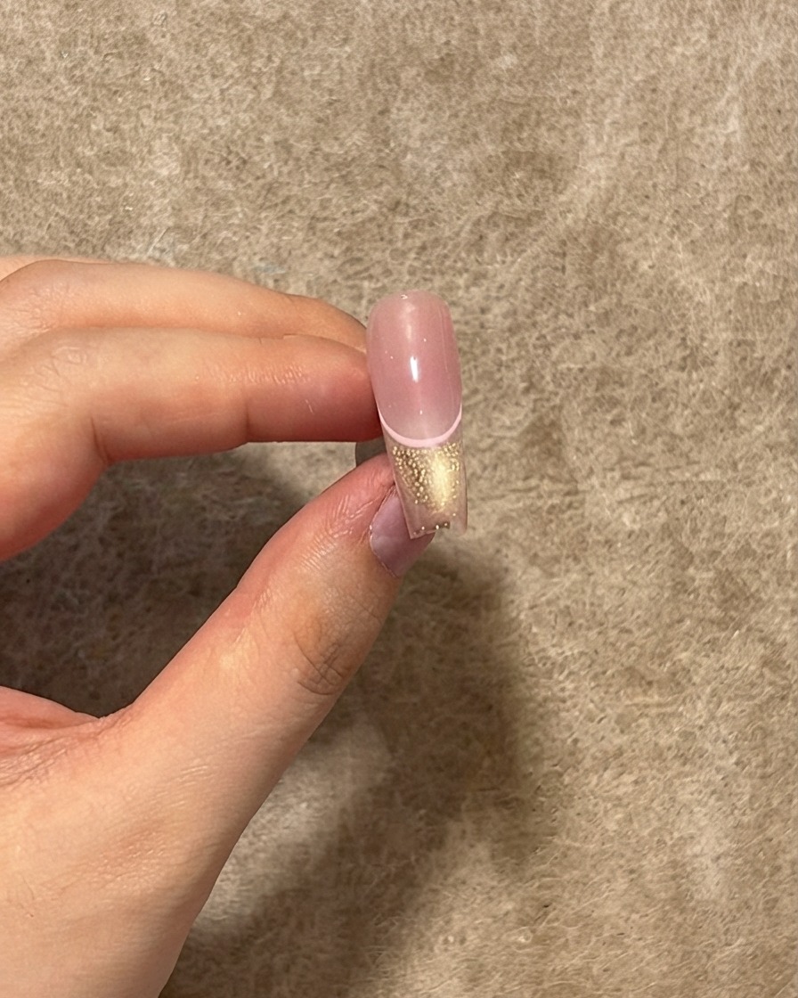 Un ongle fini montrant une couche de top coat brillant appliquée sur la ligne rose, la pointe cat eye et le centre blush.