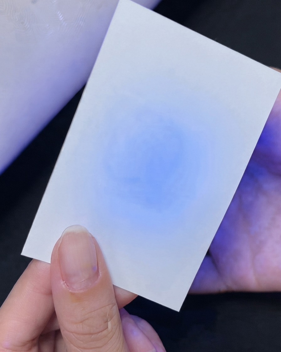 Une main tenant une carte blanche montrant un test de réflexion de lumière bleue UV en dessous.