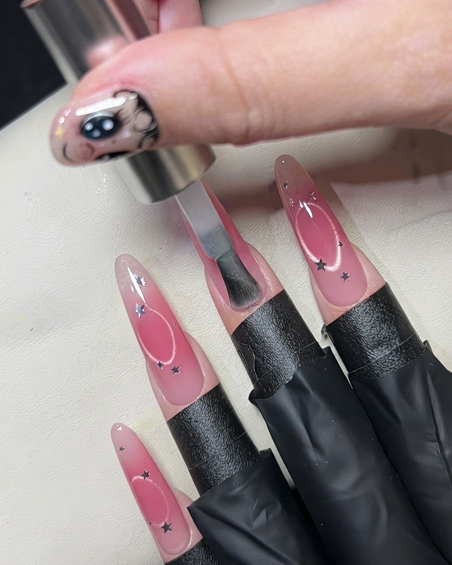 Un pinceau appliquant une couche transparente sur un ongle décoré de sequins détoiles.