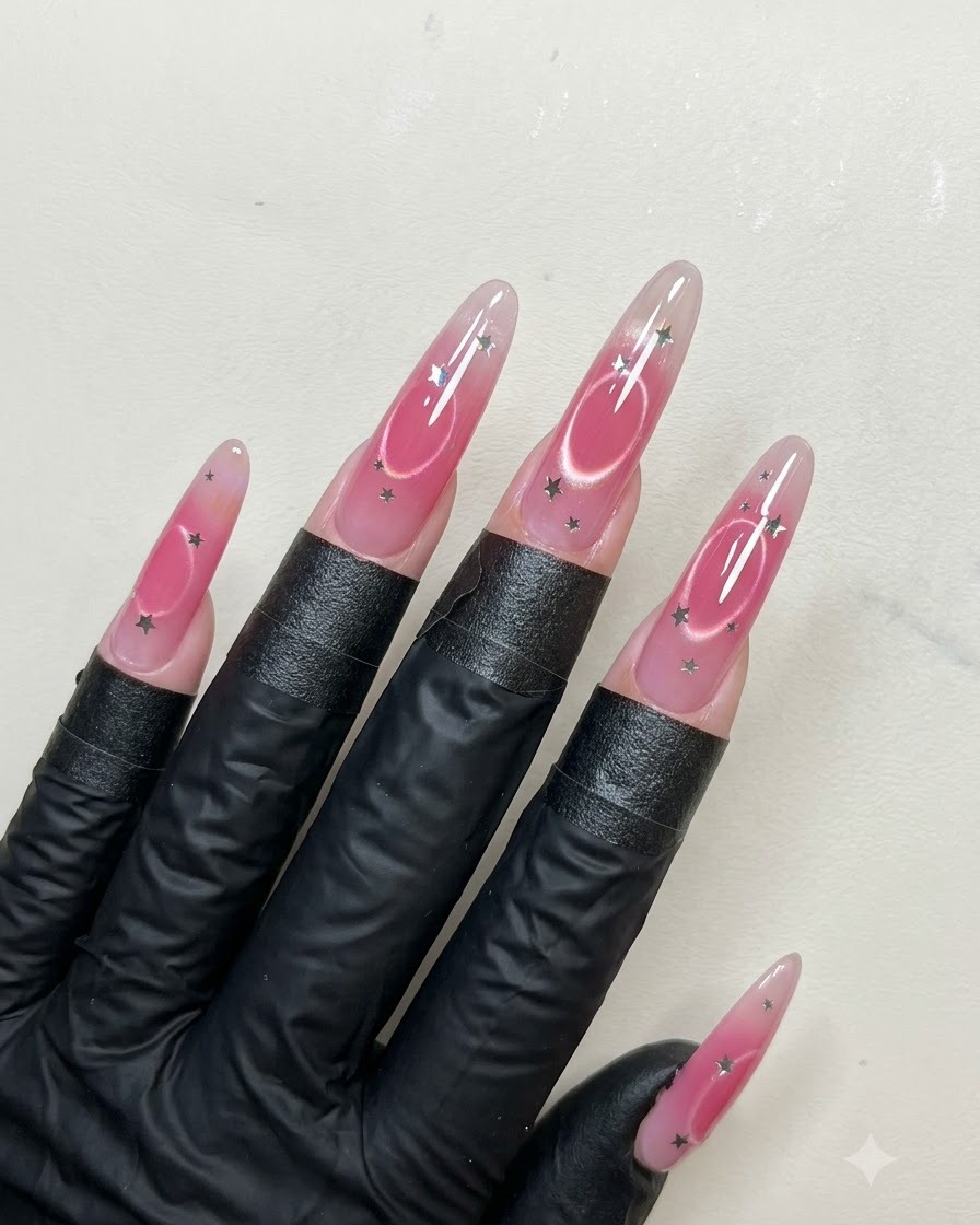 Un pinceau à ongles appliquant une couche lisse de top coat brillant sur de longs ongles en amande décorés de sequins détoiles et de nail art œil de chat.