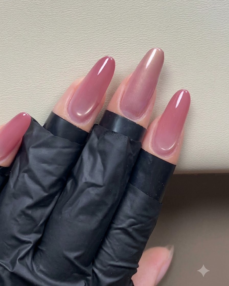 Une main tenant un aimant stylo près dun ongle œil de chat rose doré brillant pour façonner un effet de lumière latérale.