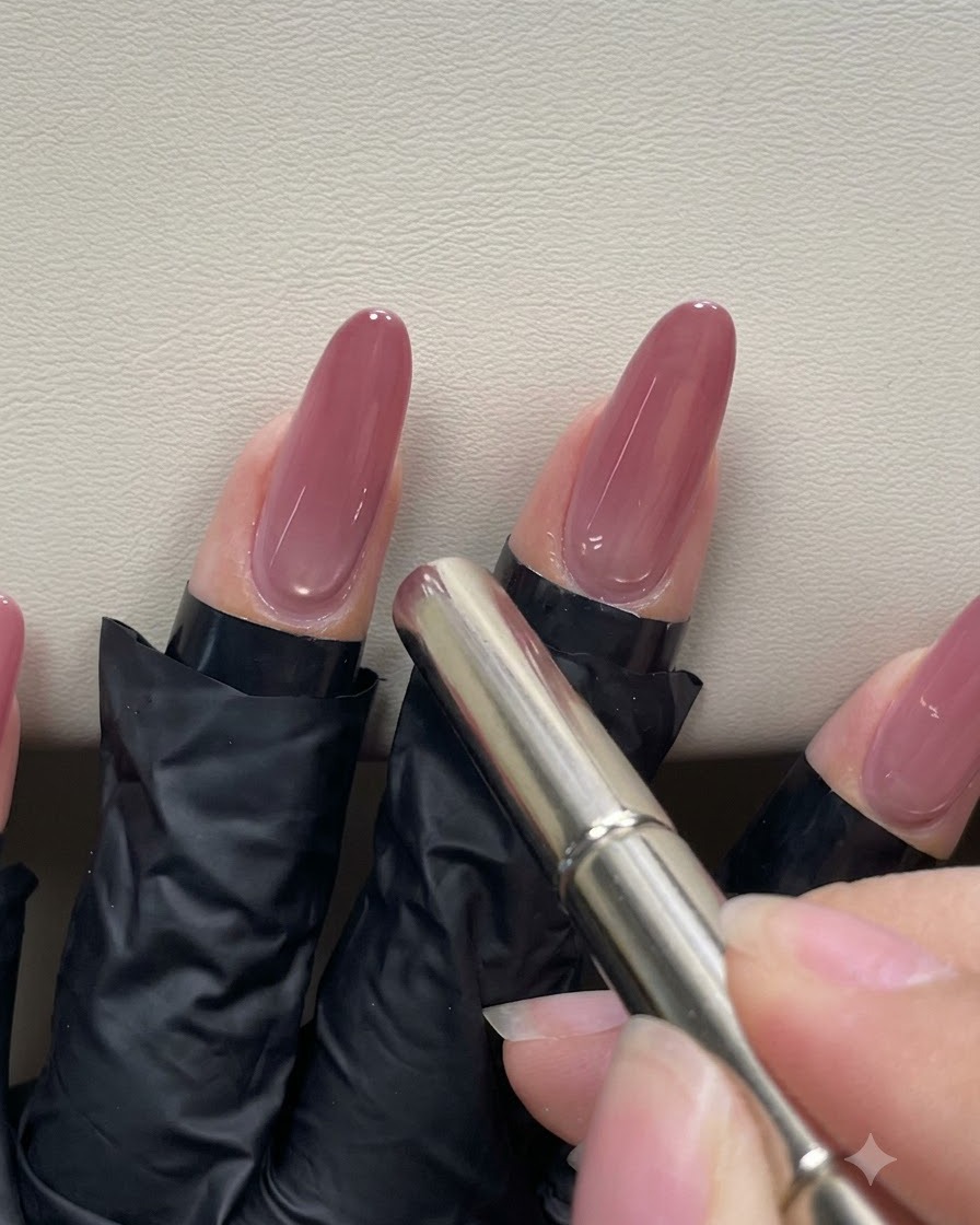 Une main utilisant un aimant stylo cylindrique, le faisant planer près de la cuticule dun ongle en gel rose pêche pour manipuler le reflet magnétique œil de chat.