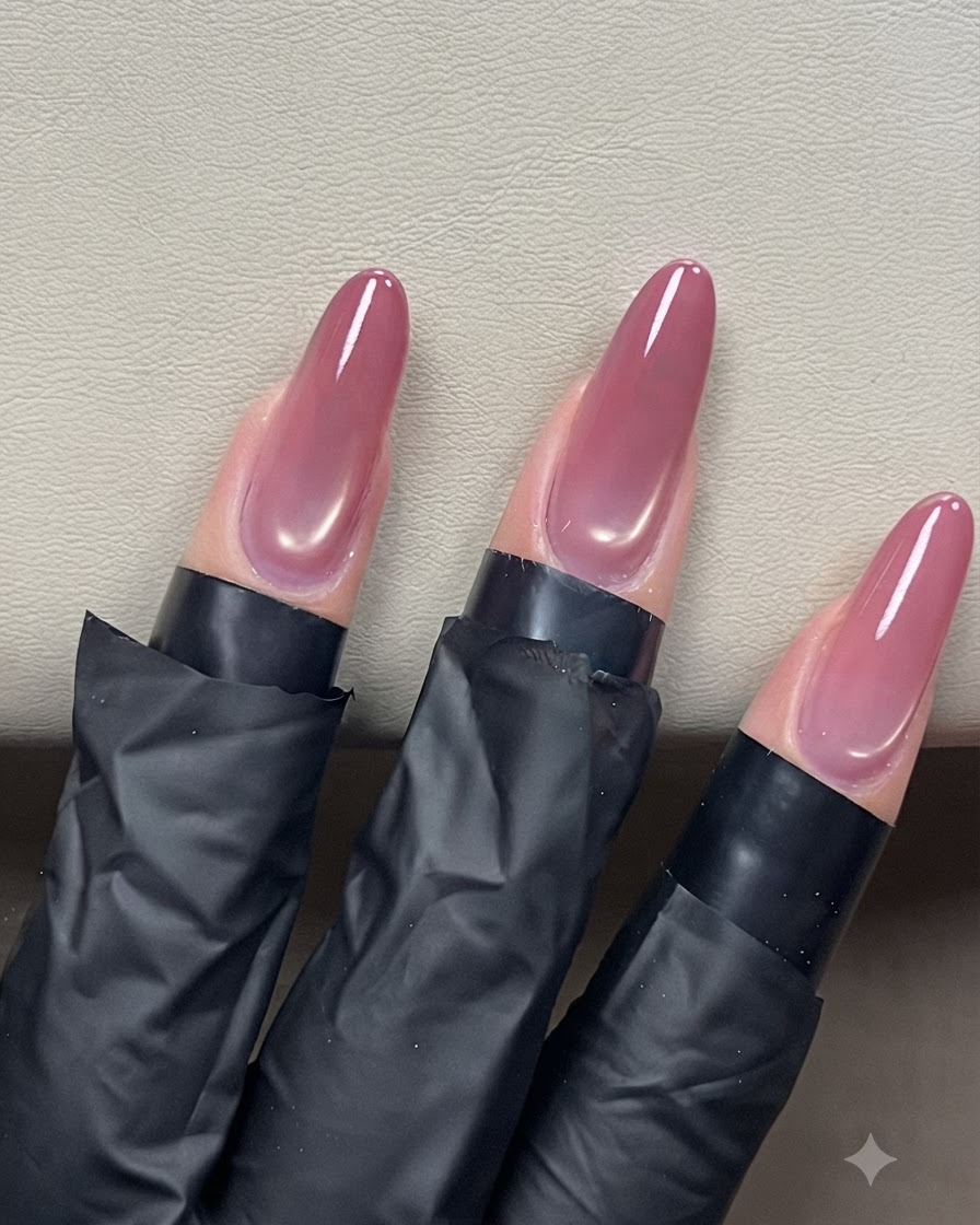 Un pinceau à ongle faisant glisser un top coat transparent sur des ongles en amande œil de chat pour une finition brillante.